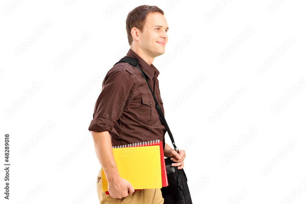 A male student with shoulder bag holding books and walking A male student with shoulder bag holding books and walking