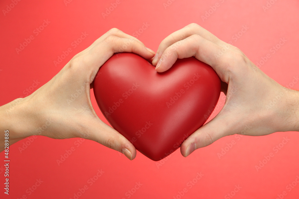 Red heart in woman and man hands, on red background Red heart in woman and man hands, on red background