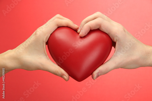 Red heart in woman and man hands  on red background