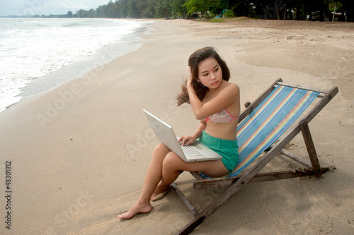Pretty Thai woman working at laptop on bed beach.