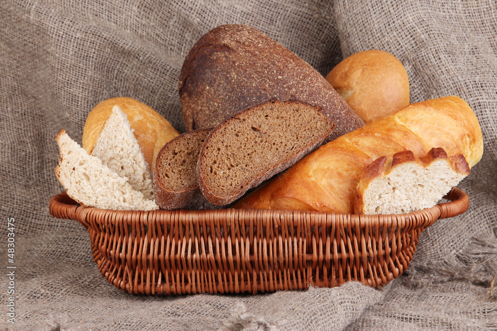 Fresh bread in basket on wooden table on sacking background