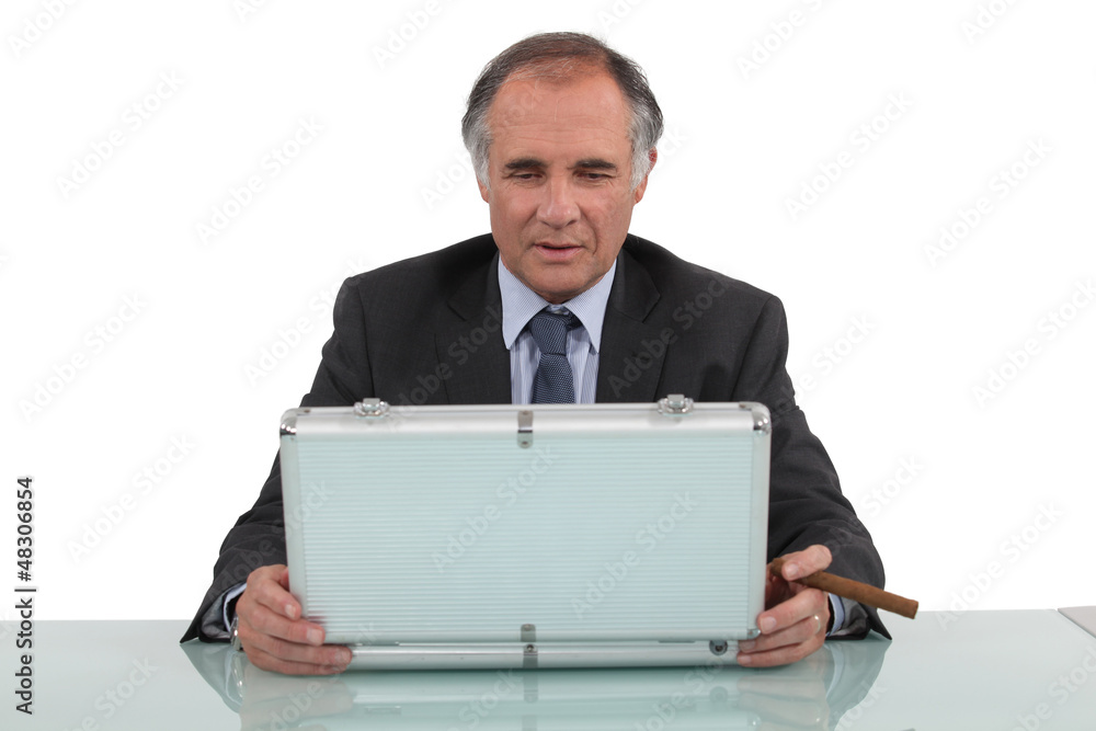 A businessman looking in a briefcase and smoking a cigar. A businessman looking in a briefcase and smoking a cigar.