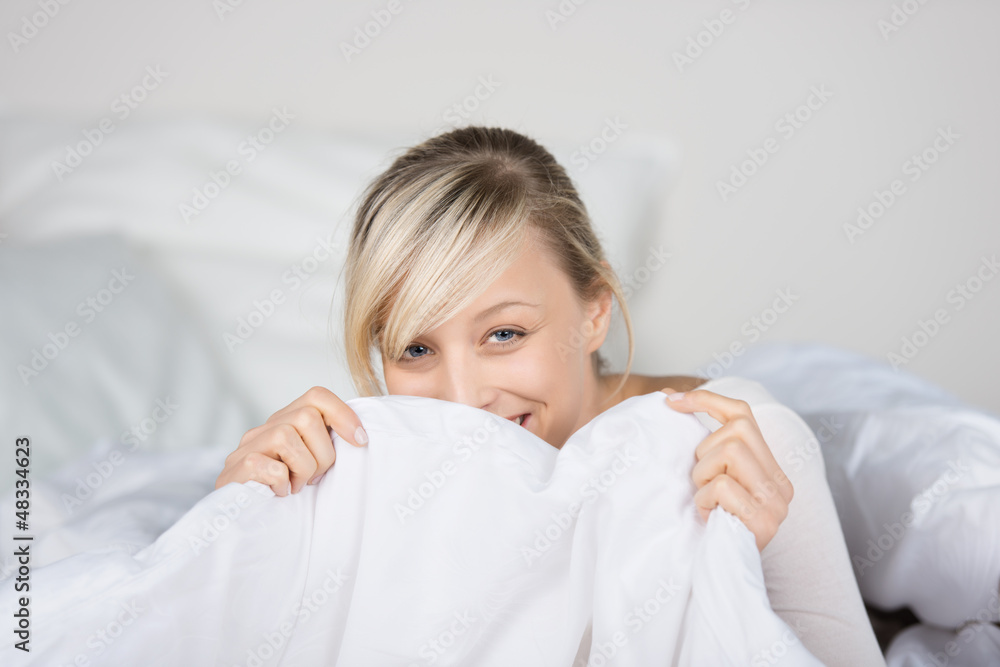 lachende frau versteckt sich hinter bettdecke lachende frau versteckt sich hinter bettdecke