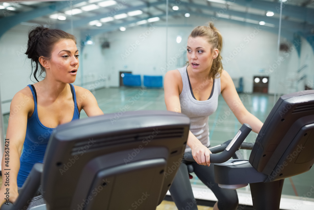 Two women working out on exercise bikes Two women working out on exercise bikes