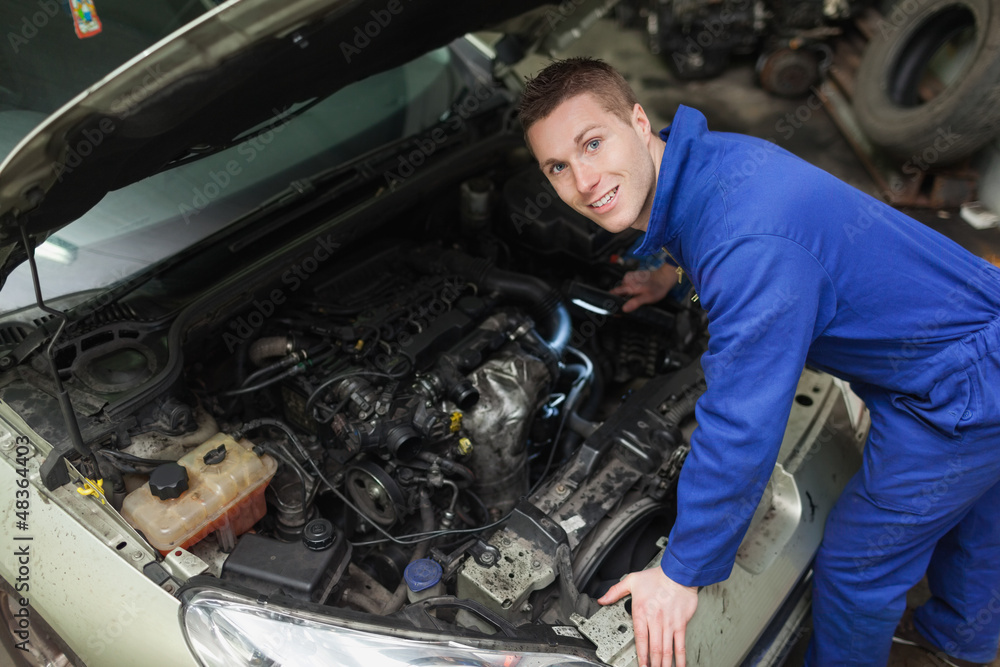 Happy mechanic examining car engine Happy mechanic examining car engine