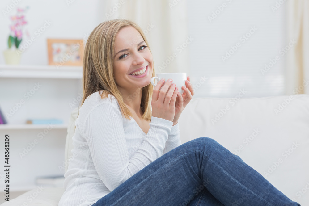 Smiling woman with coffee cup sitting on couch Smiling woman with coffee cup sitting on couch