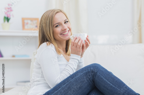 Smiling woman with coffee cup sitting on couch