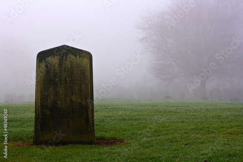 Single gravestone in a spooky graveyard on a foggy day