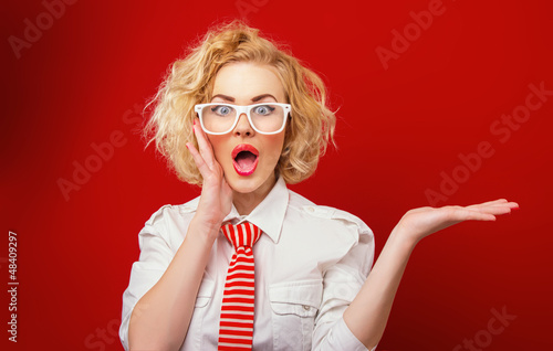 Surprised woman showing product, isolated on red background