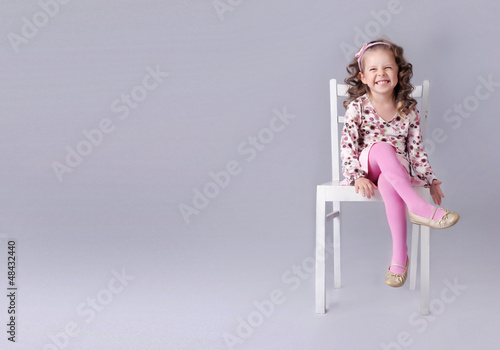 Cheerful little girl sitting on the chair with smile