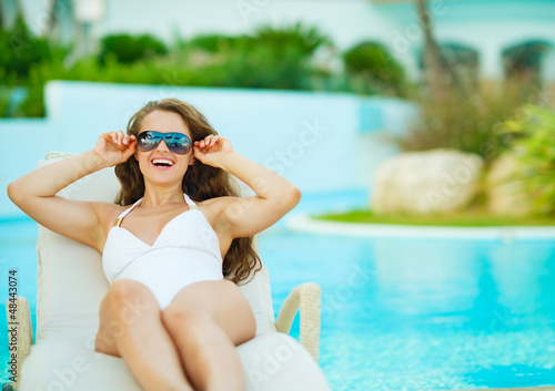 Happy young woman in swimsuit relaxing on chaise-longue