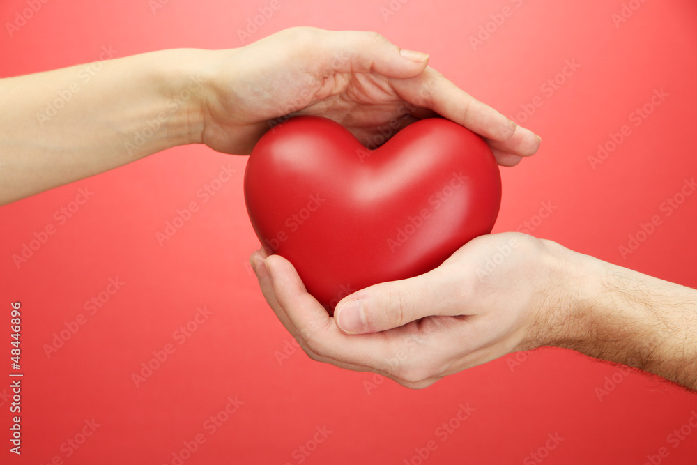 Red heart in woman and man hands, on red background Red heart in woman and man hands, on red background