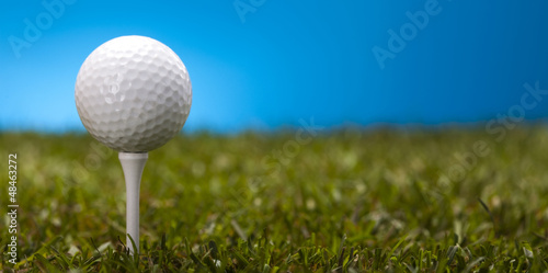 Golf ball on green grass over a blue background 