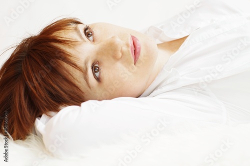 The happy young woman lying on a white fur plaid