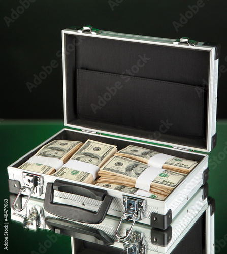 Suitcase with 100 dollar bills on dark color background