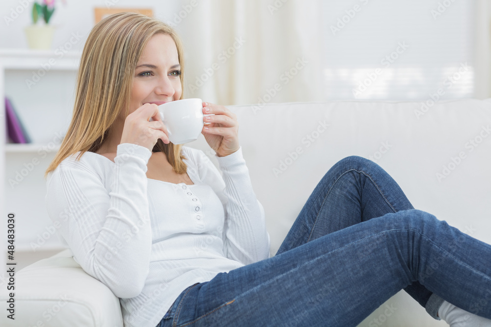 Woman drinking coffee as she looks away on couch