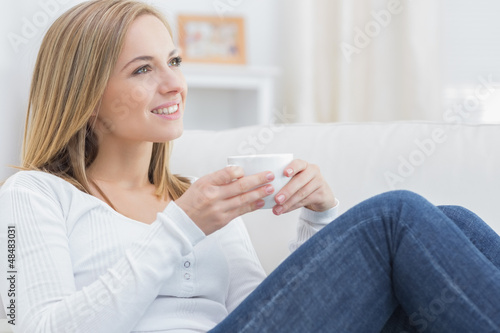 Woman with coffee cup day dreaming on couch