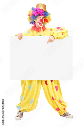 Full length portrait of a happy male clown pointing on a panel photo