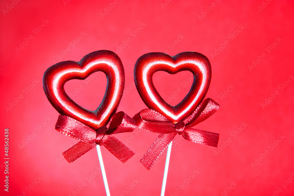 two red valentine hearts with bows against red background