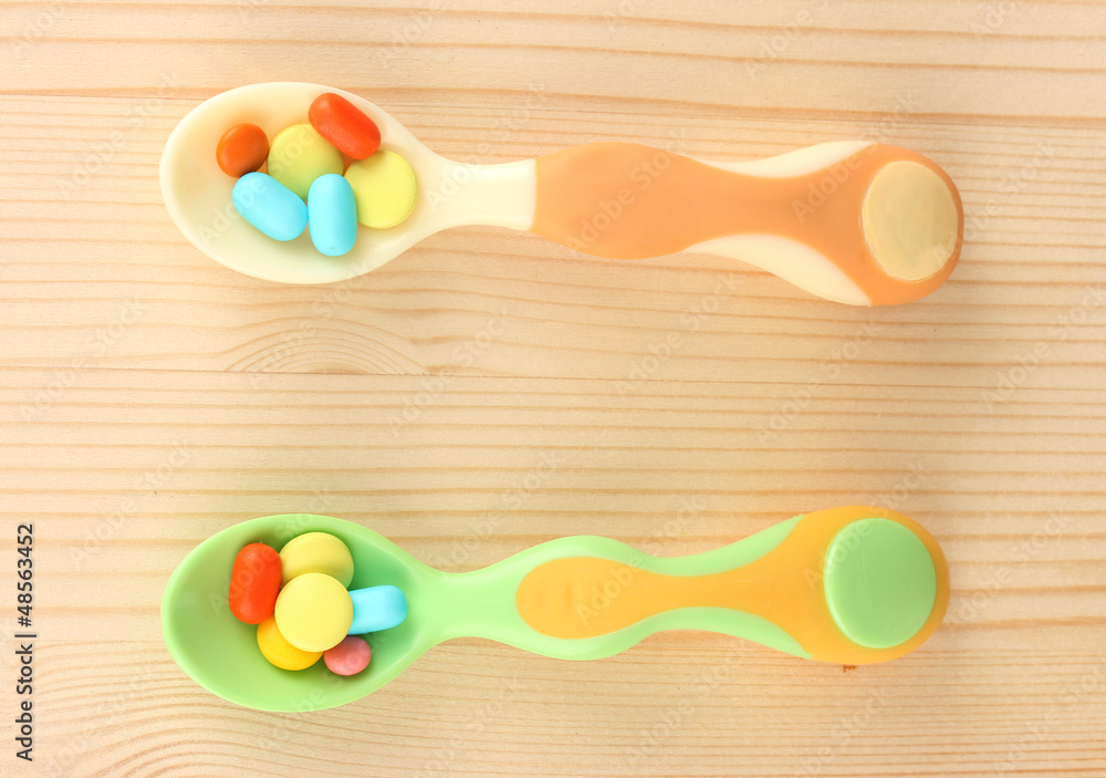 Plastic spoons with color pills on wooden background Plastic spoons with color pills on wooden background