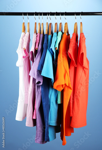Variety of casual shirts on wooden hangers on blue background