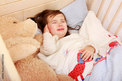 Ein kleines Mädchen liegt in seinem Bett und weint photo