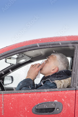 Mid aged man with flu symptoms sneezes in a car on snowy day