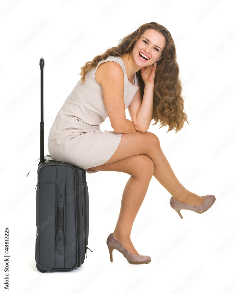 Fototapeta premium Smiling young woman sitting on wheels suitcase