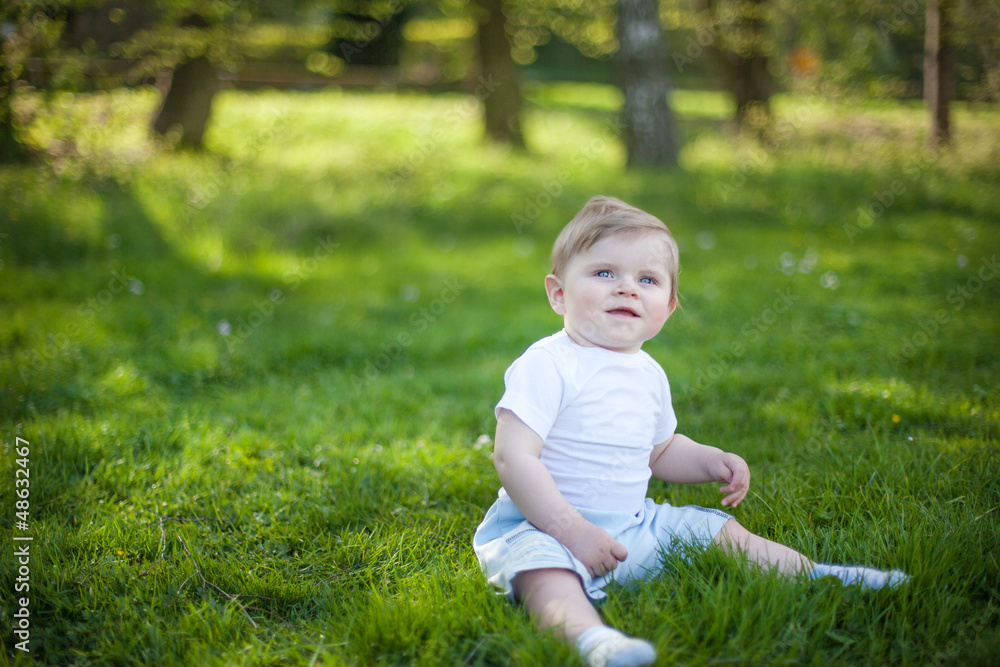 Beautiful baby boy on green grass in summer