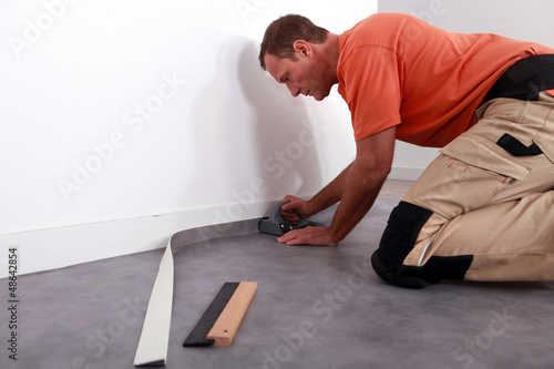 Foto Man putting down linoleum on a baseboard