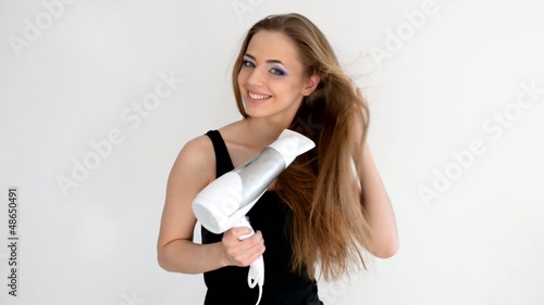 Beautiful smiling girl drying her hair with a blow dryer