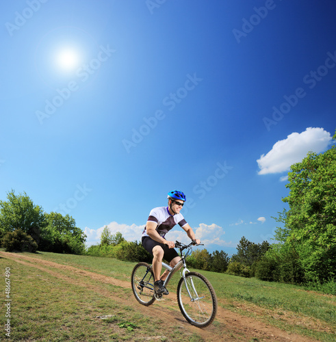 Male bicyclist riding a mountain bike down hill on a sunny day