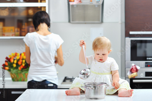 Little girl cooking on a kitchen with mother in the background