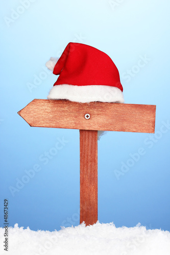 Wooden road sign with Santa hat on blue background