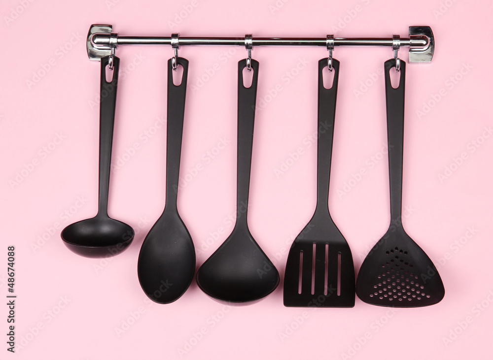 Black kitchen utensils on silver hooks, on pink background Black kitchen utensils on silver hooks, on pink background