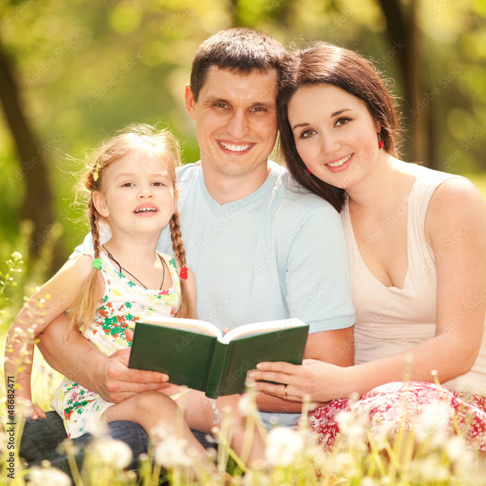 Happy mother, father and daughter read a book in the park Happy mother, father and daughter read a book in the park