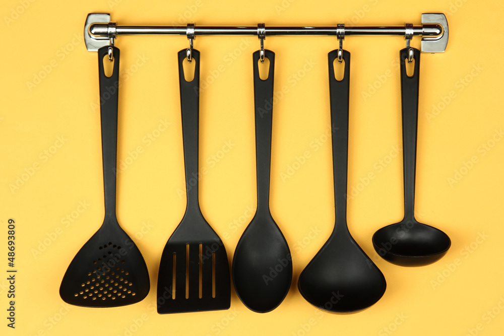 Black kitchen utensils on silver hooks, on yellow background Black kitchen utensils on silver hooks, on yellow background