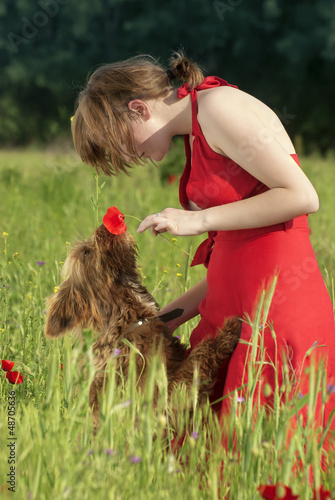 Beautiful scene of a girl in red dress, playing with her dog and giving him flower to smell 