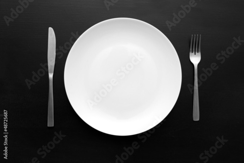 empty white plate with fork and knife on dark wooden table
