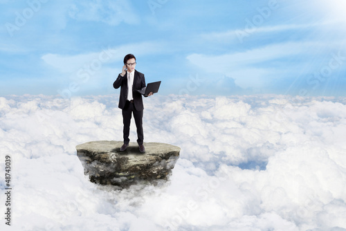 Businessman working with laptop above clouds