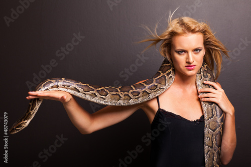 sexy young woman holding a python on black background