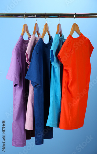 Variety of casual shirts on wooden hangers on blue background
