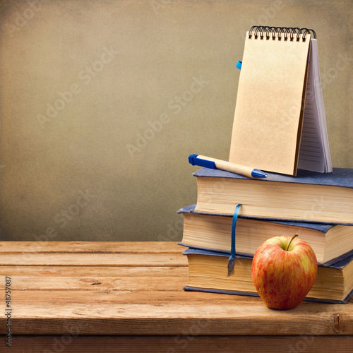 Old books with apple and note book on wooden table.