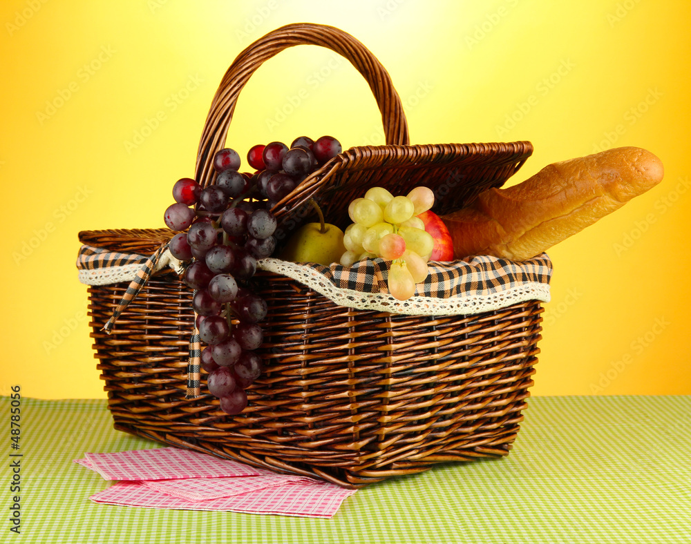 Picnic basket with fruits on cloth on yellow background Picnic basket with fruits on cloth on yellow background