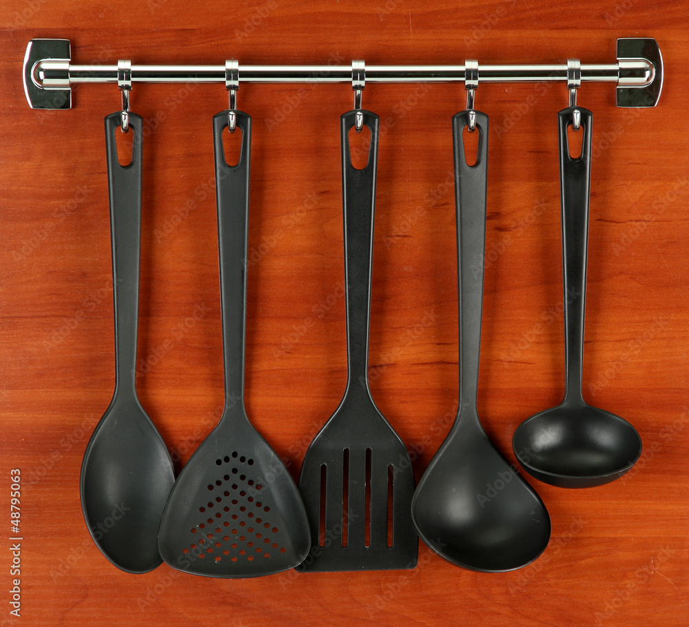 Black kitchen utensils on silver hooks, on wooden background Black kitchen utensils on silver hooks, on wooden background