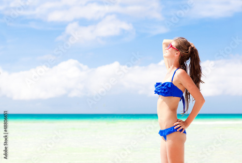Beautiful young woman standing on the beach enjoying the sun