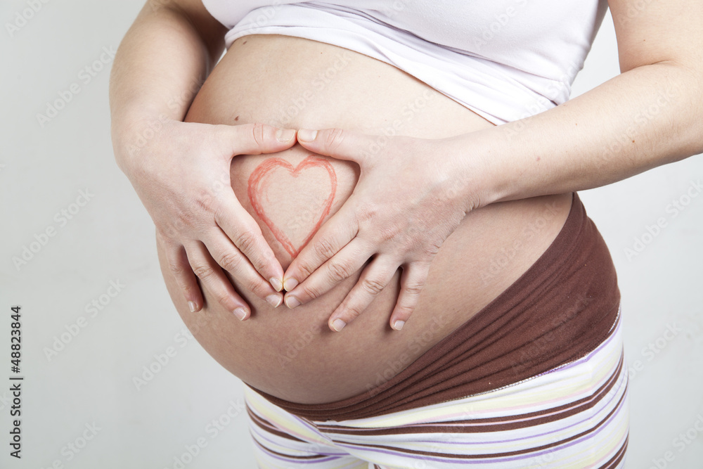 Pregnant woman making heart shape with hands over her stomach Pregnant woman making heart shape with hands over her stomach