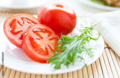 Ripe tomato on a white plate and salad leaves