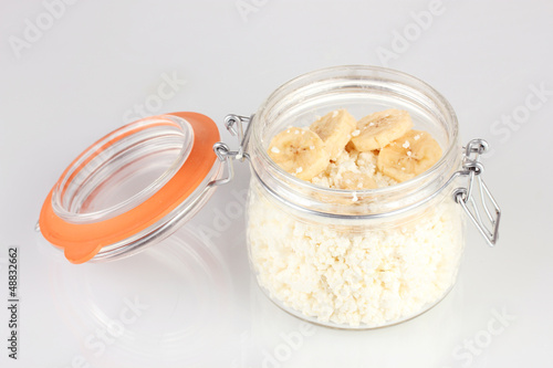 Cottage cheese in glass bottle with banana, isolated on white