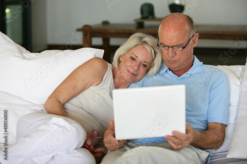 Middle-aged couple sat on sofa with laptop
